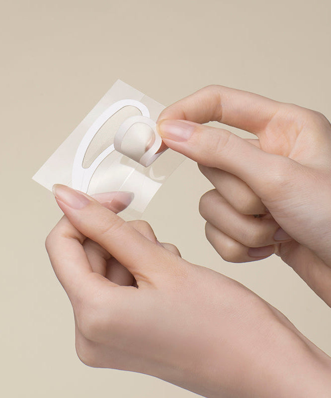 Hands peeling off NEEDLY Eye Patch from its packaging on a neutral background.