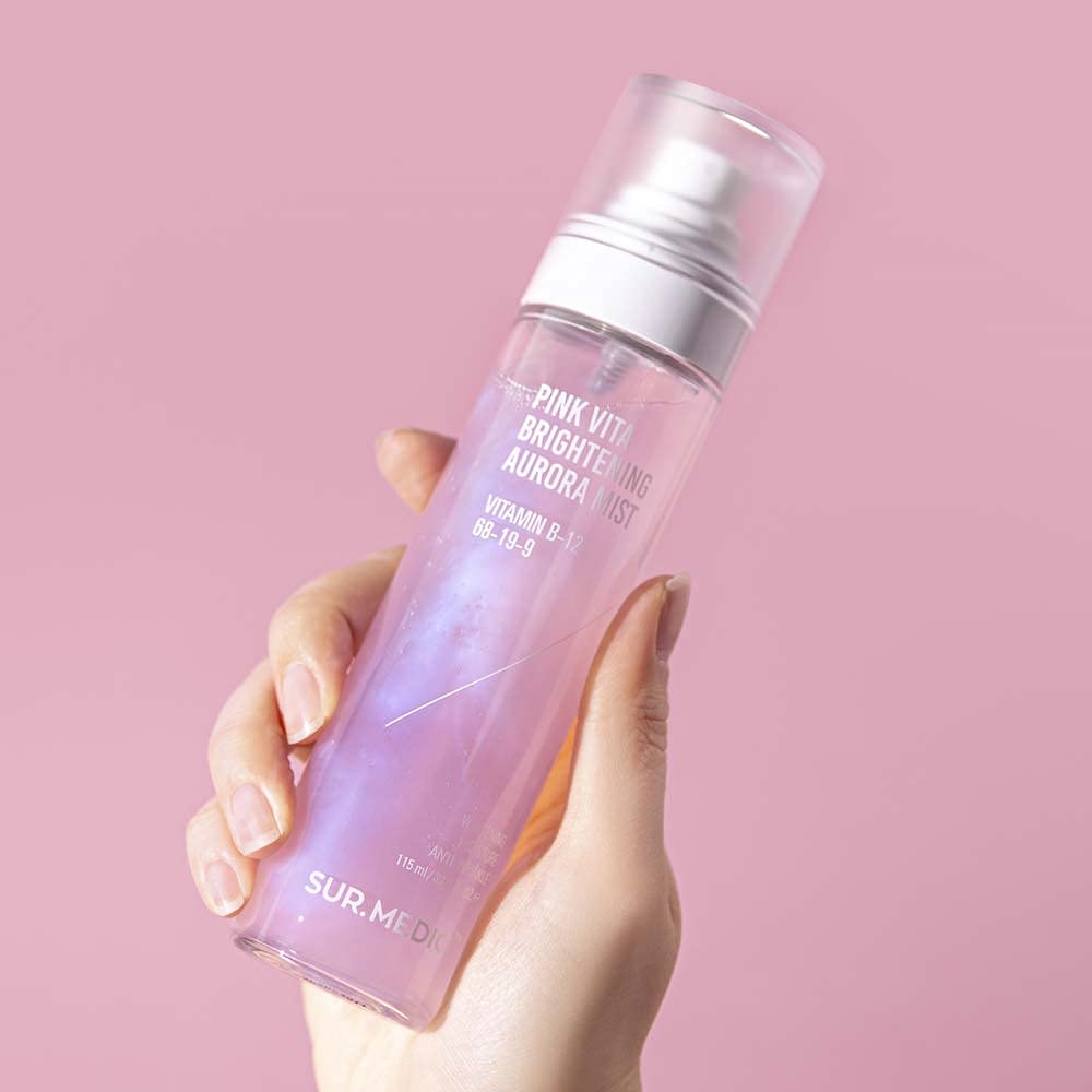 Hand holding NEOGEN Pink Vita Aurora Mist 115ml against a pink background