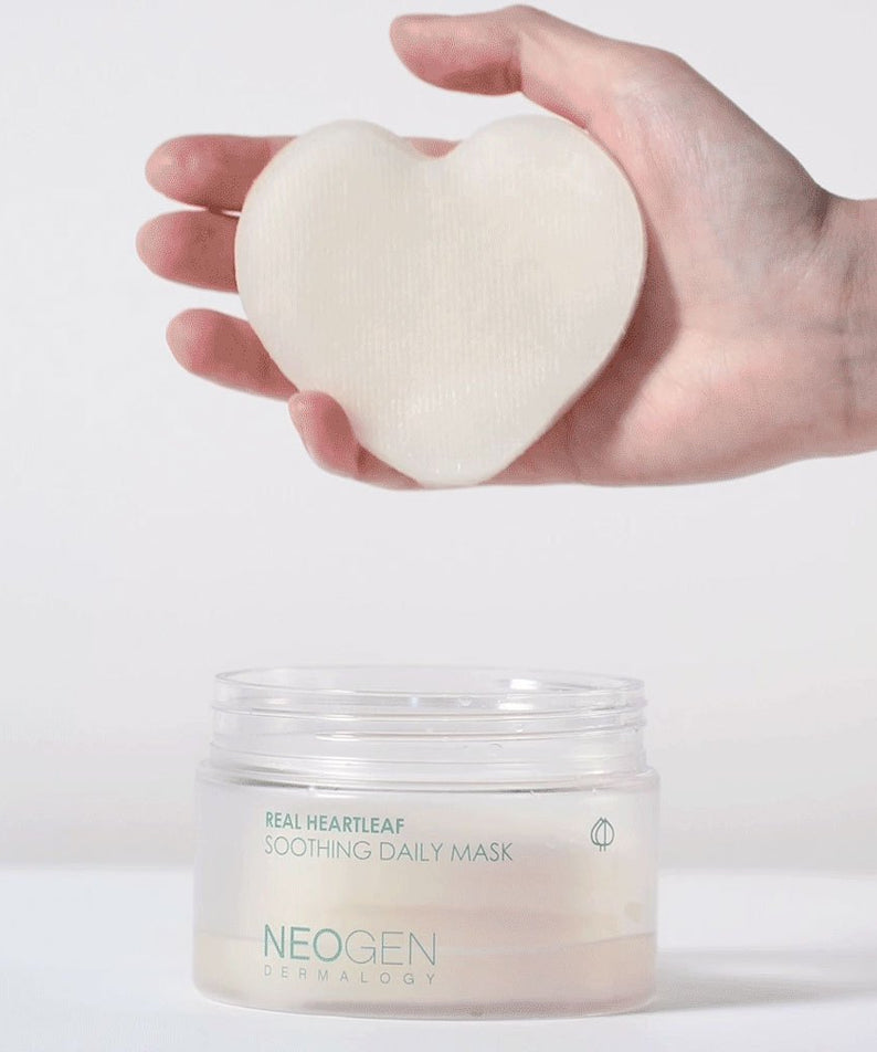 Hand holding NEOGEN Real Heartleaf Soothing Daily Mask 40 Sheets above open jar, showcasing heart-shaped pad for skincare.