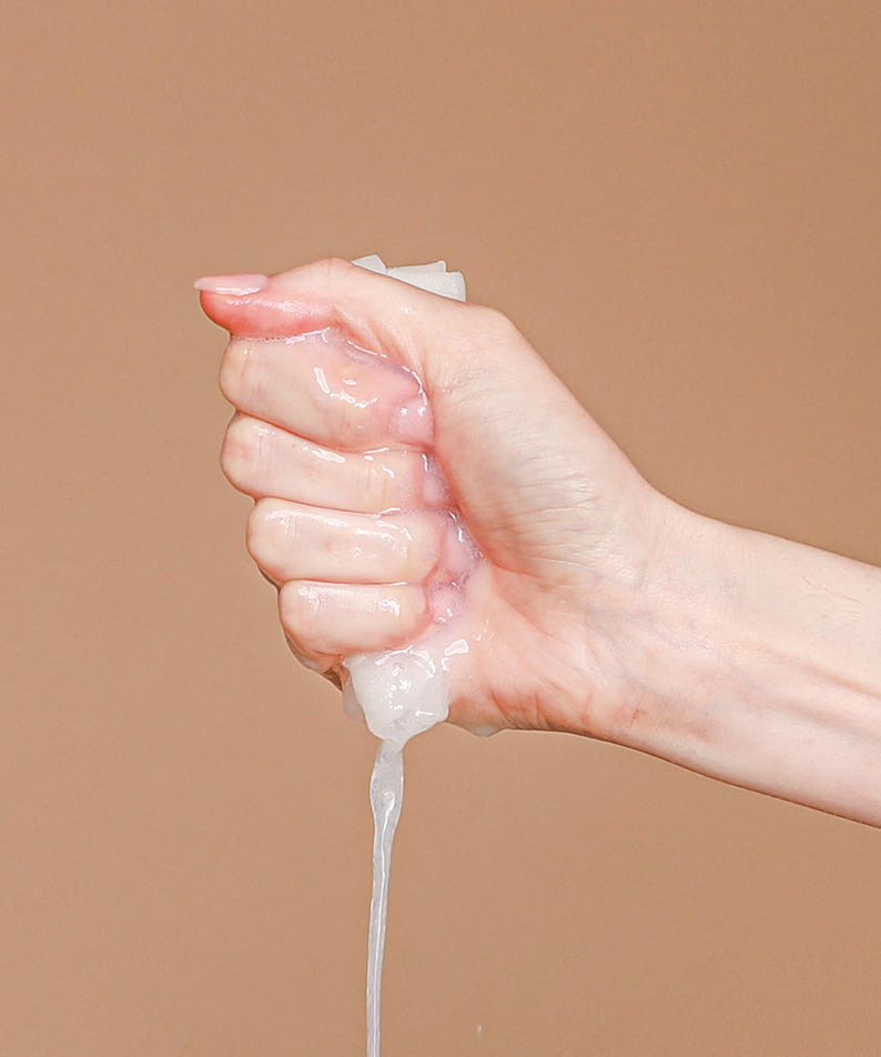 Hand squeezing liquid from NEOGEN Real Heartleaf Soothing Mask 5 Packs, demonstrating product texture on a beige background.
