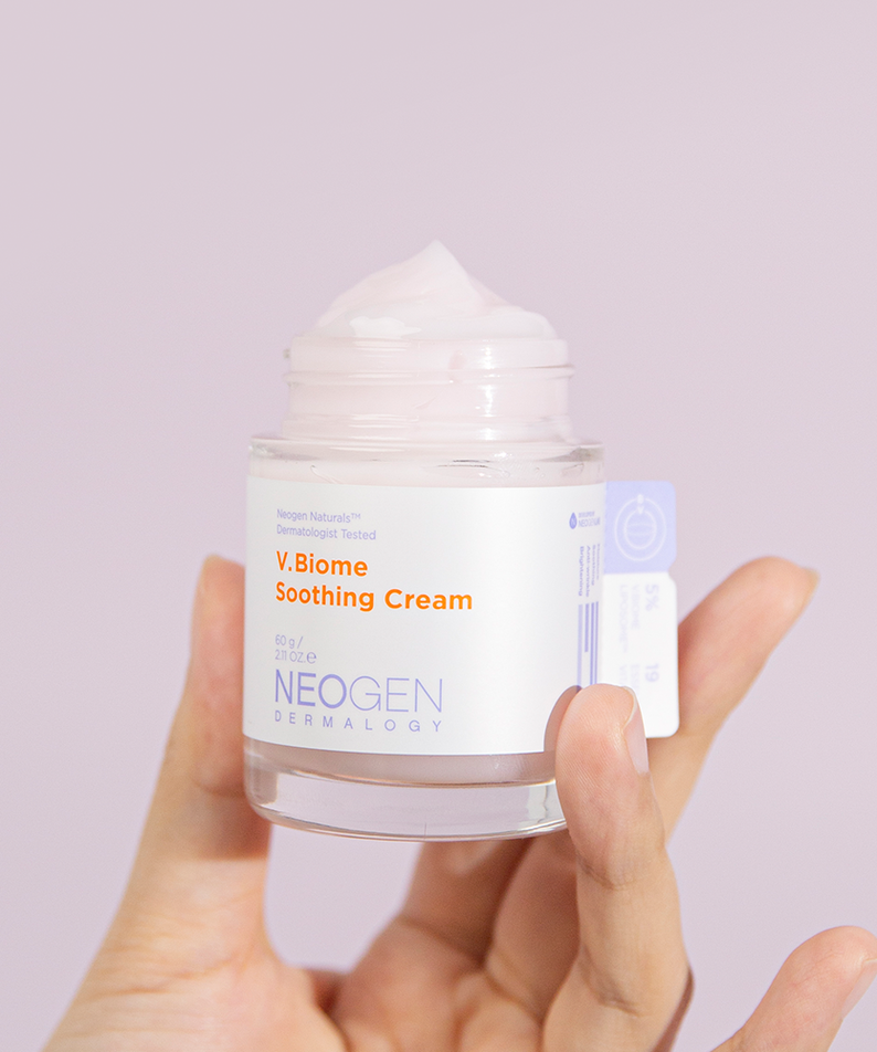 Hand holding NEOGEN V Biome Soothing Cream 60g jar with pink cream against a light background.