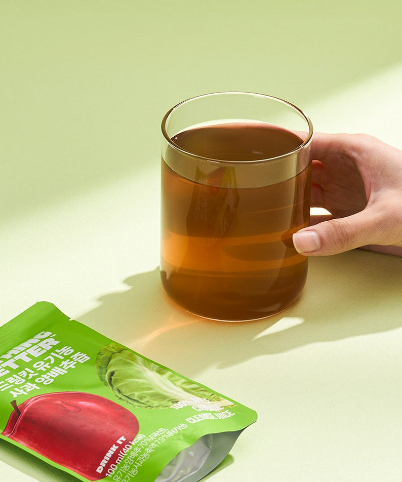 NOTHING BETTER Drinkit Organic Applr Cabbage Juice 100ml 24 Packets with a glass of juice and packet on a table.