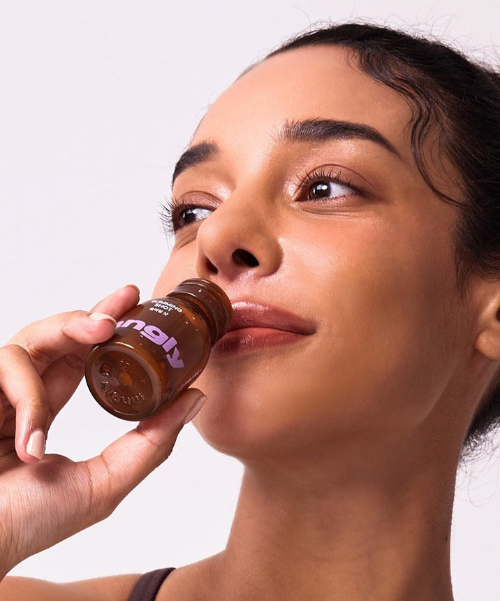Woman enjoying a NOTHING BETTER Tangly Slimming Shot bottle, promoting wellness and slimming benefits.