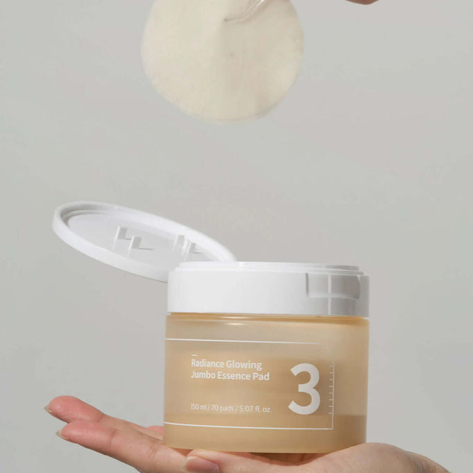 NUMBUZIN No.3 Radiance Glowing Jumbo Essence Pad in a hand, lid open with essence pad being lifted, showcasing product design and packaging.