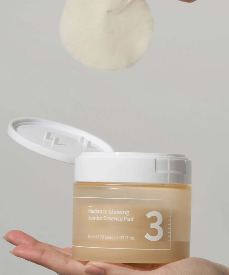 NUMBUZIN No.3 Radiance Glowing Jumbo Essence Pad in a hand, lid open with essence pad being lifted, showcasing product design and packaging.