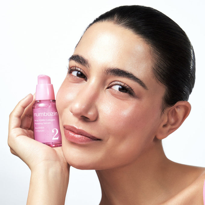 Smiling woman holding NUMBUZIN No.2 Rose PDRN Collagen Plumping Serum 30ml bottle next to her face.
