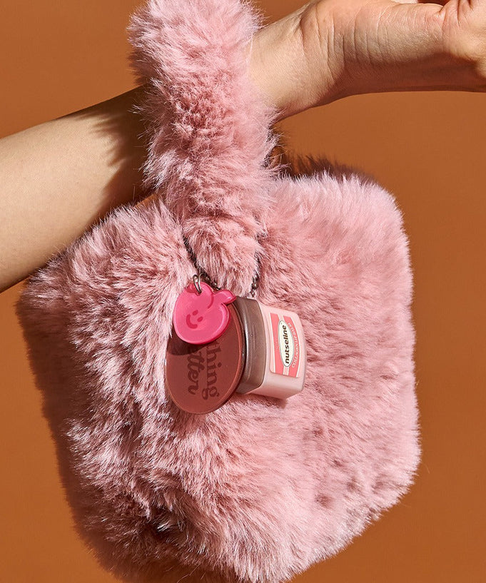 NUTSELINE Super Nut Collagen Keyring Lip Balm 11ml hanging on a pink fluffy bag held by a hand.