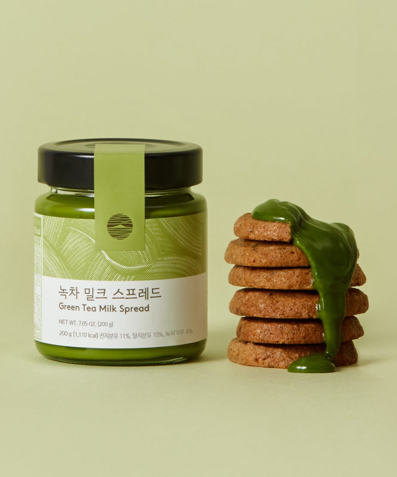 Jar of OSULLOC Green Tea Milk Spread 200g next to stack of cookies topped with green tea milk spread on light green background.