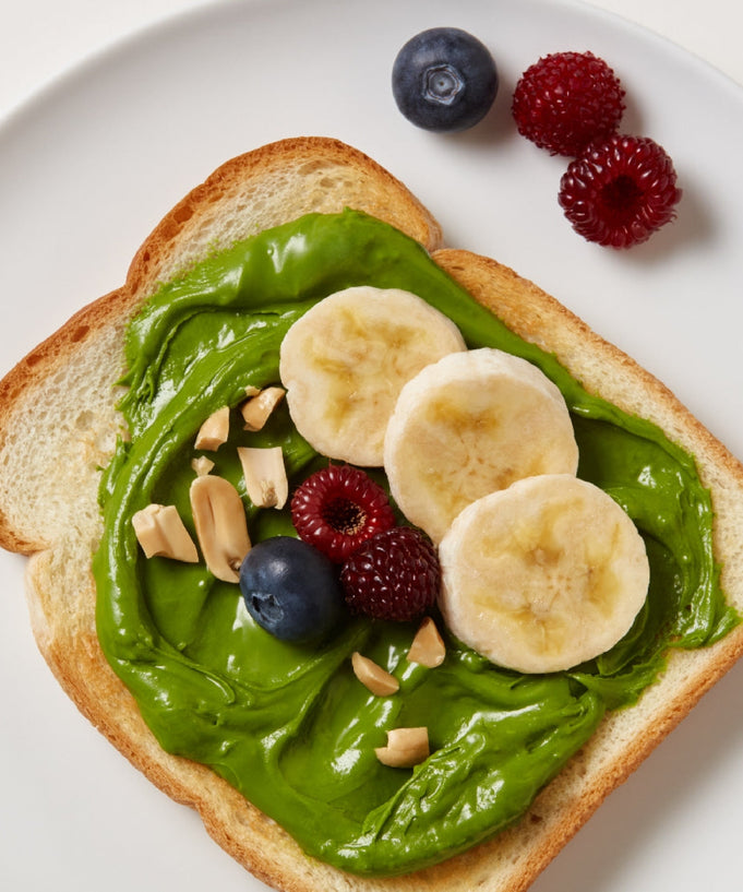Toast topped with OSULLOC Green Tea Milk Spread 200g, banana slices, and mixed berries on a white plate.