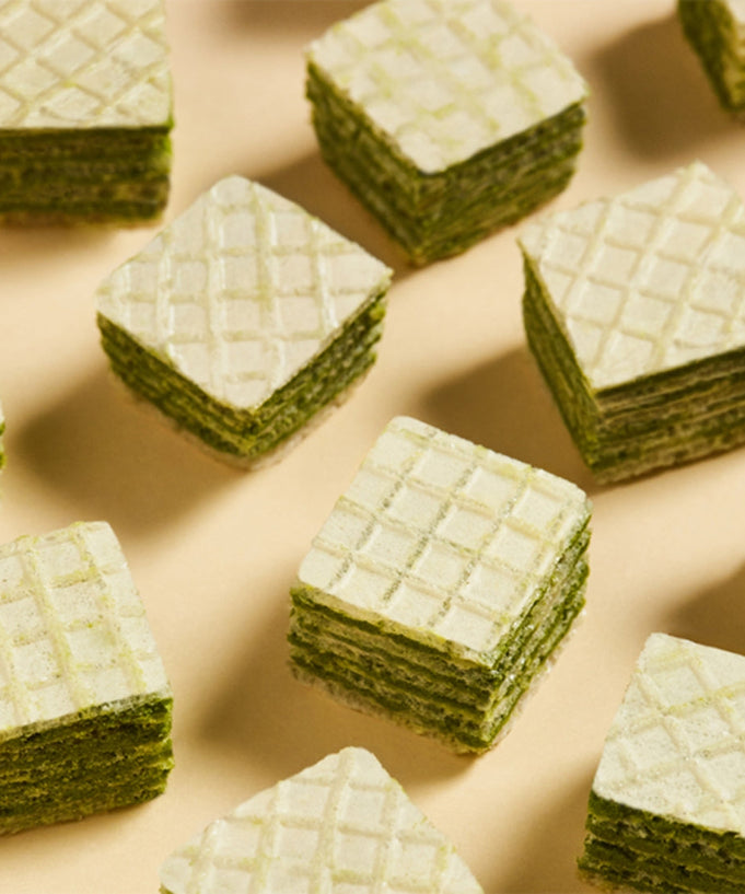 OSULLOC Green Tea Wafers 100g arranged in a grid pattern on a beige surface, showcasing layers and texture.