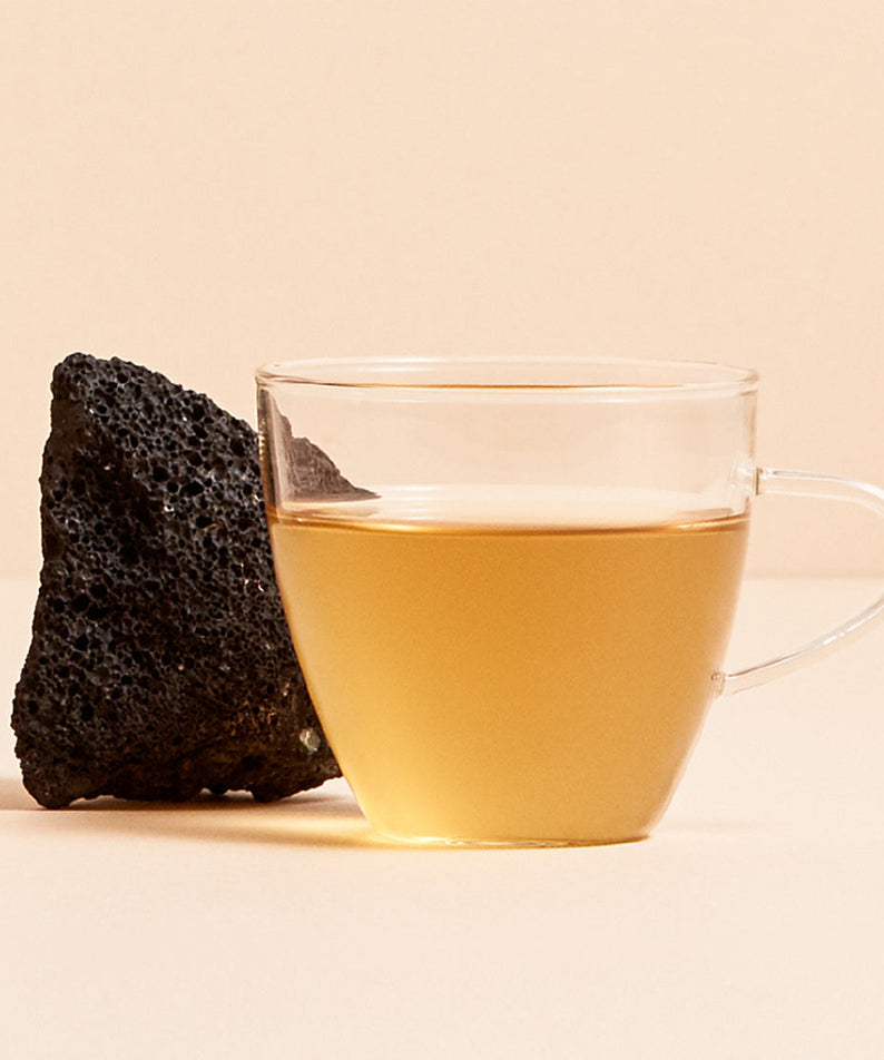 Glass cup of OSULLOC Jeju Volcanic Oolong Tea with volcanic rock behind on neutral background