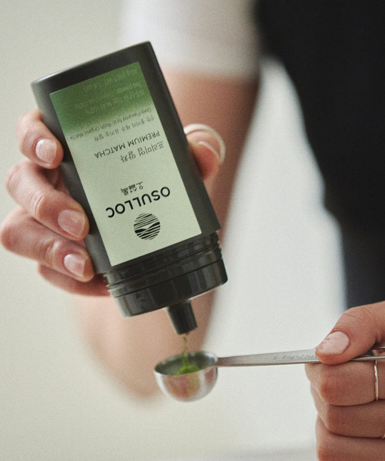 Person pouring OSULLOC Premium Matcha 40g into a measuring spoon, highlighting the premium quality of the matcha tea powder.