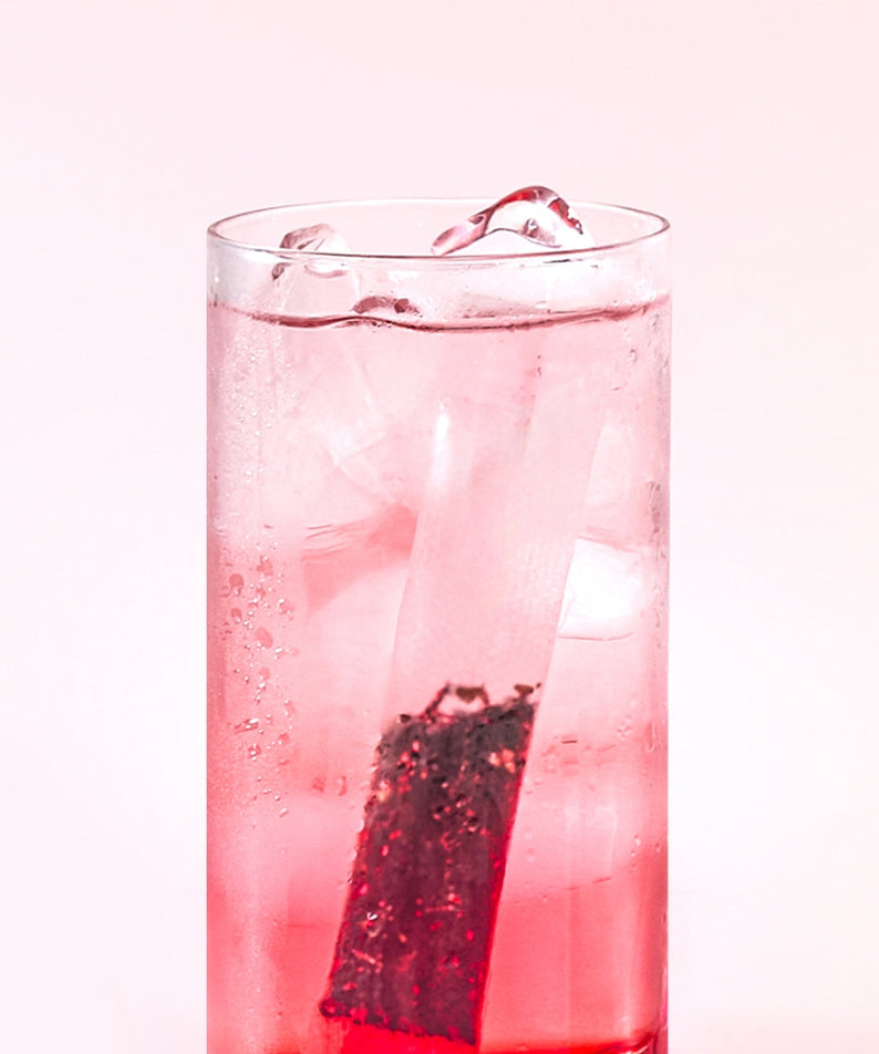 Glass of refreshing OSULLOC Sweet Hibiscus Cold Brew Tea 20 P with ice cubes and a tea bag, showcasing the pink hue of the drink.