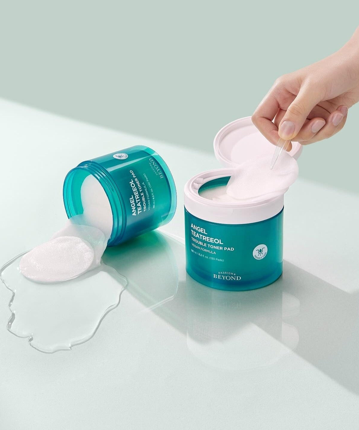 PASSION&BEYOND Angel Tea Tree Trouble Toner Pads 185ml skincare product with open lid and spilled pads on a light surface.