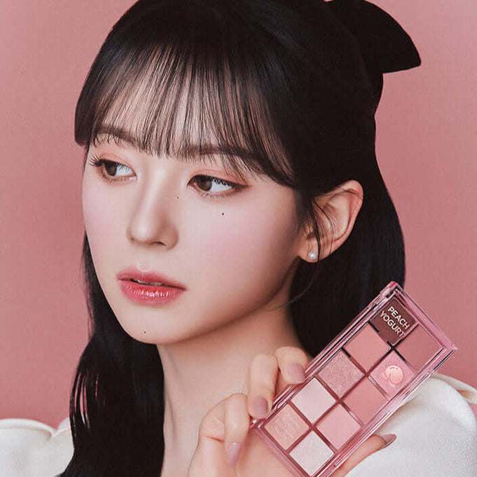 Model holding PEACH C Seasonal Blending Eyeshadow Palette (Sweet Topping) against a pink background, showcasing makeup shades.