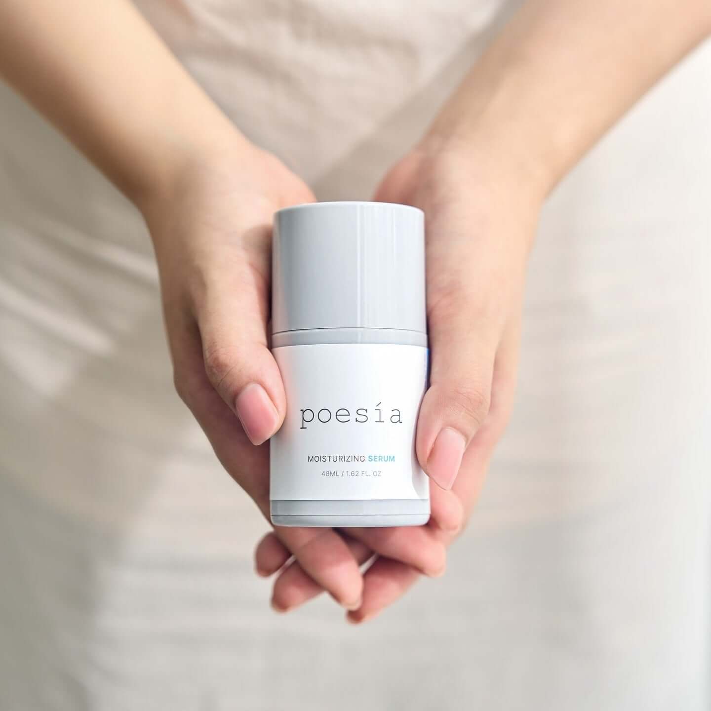 Hands holding POESÃA Hydro Hyaluronic Deep Moisturizing Ampoule Serum 48ml bottle.