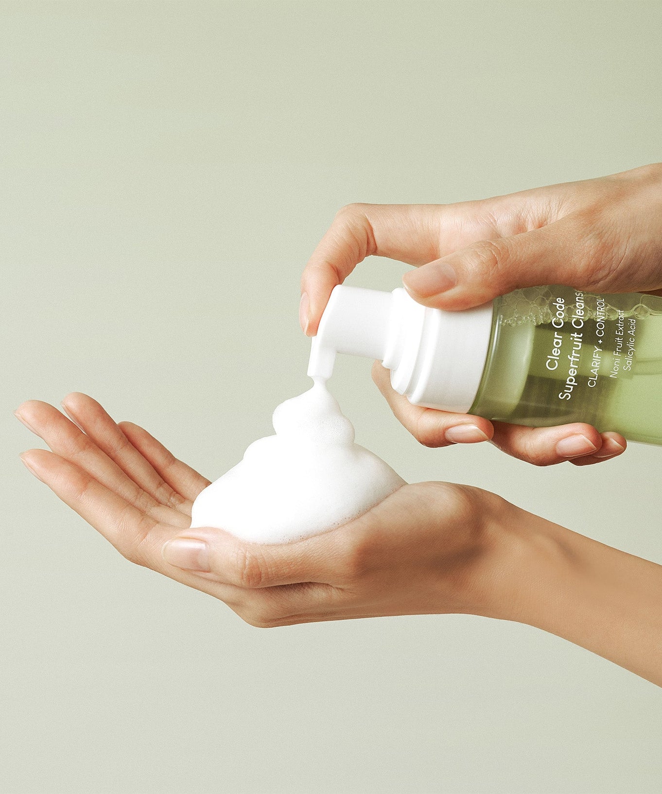 Hands using PURITO Clear Code Superfruit Cleanser 150ml, dispensing foamy cleanser into palm.