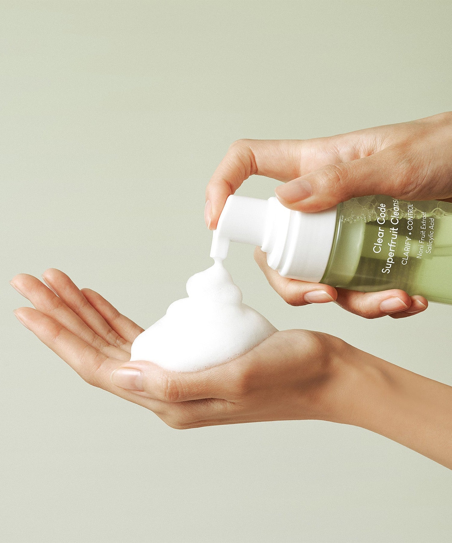 Hands using PURITO Clear Code Superfruit Cleanser 150ml, dispensing foamy cleanser into palm.
