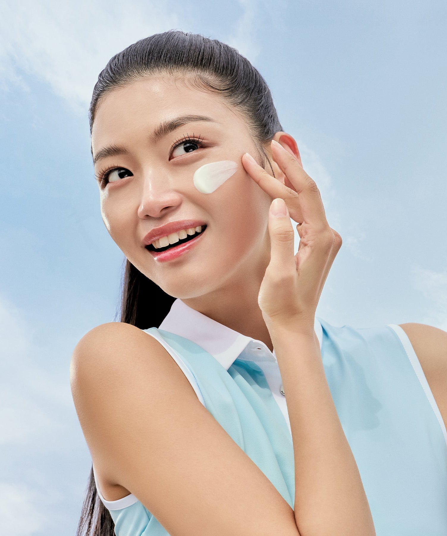 Smiling woman applying PURITO Daily Soft Touch Sun Cream SPF50+PA++++ under blue sky background.