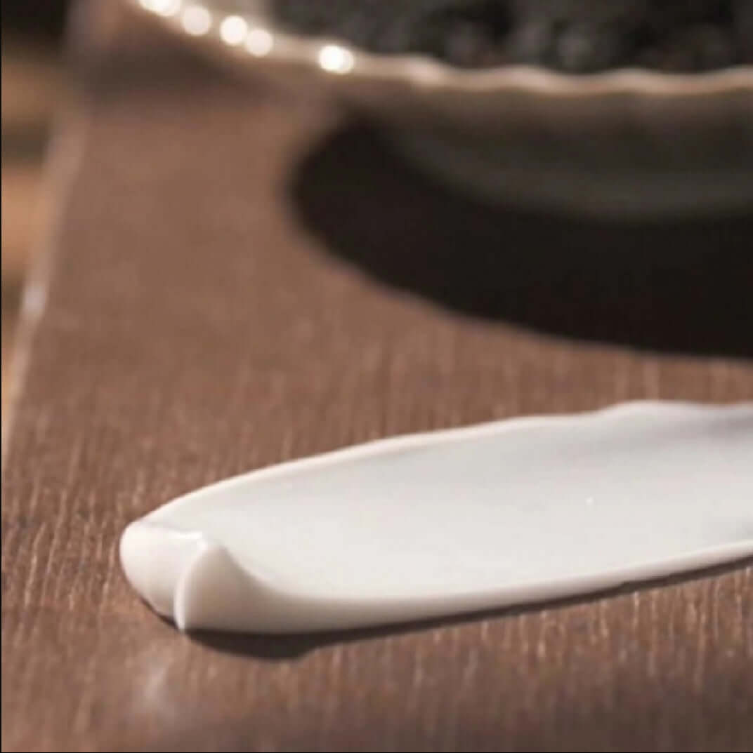 Texture of PYUNKANG YUL Black Tea Enriched Cream 60ml displayed on a wooden surface.