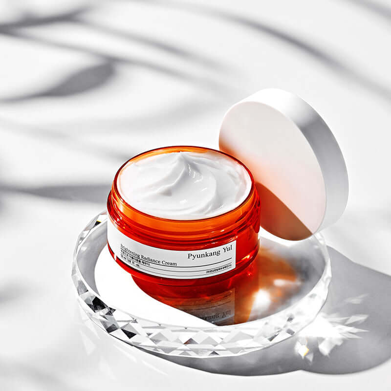 Open jar of PYUNKANG YUL Brightening Radiance Cream 50ml on a reflective surface