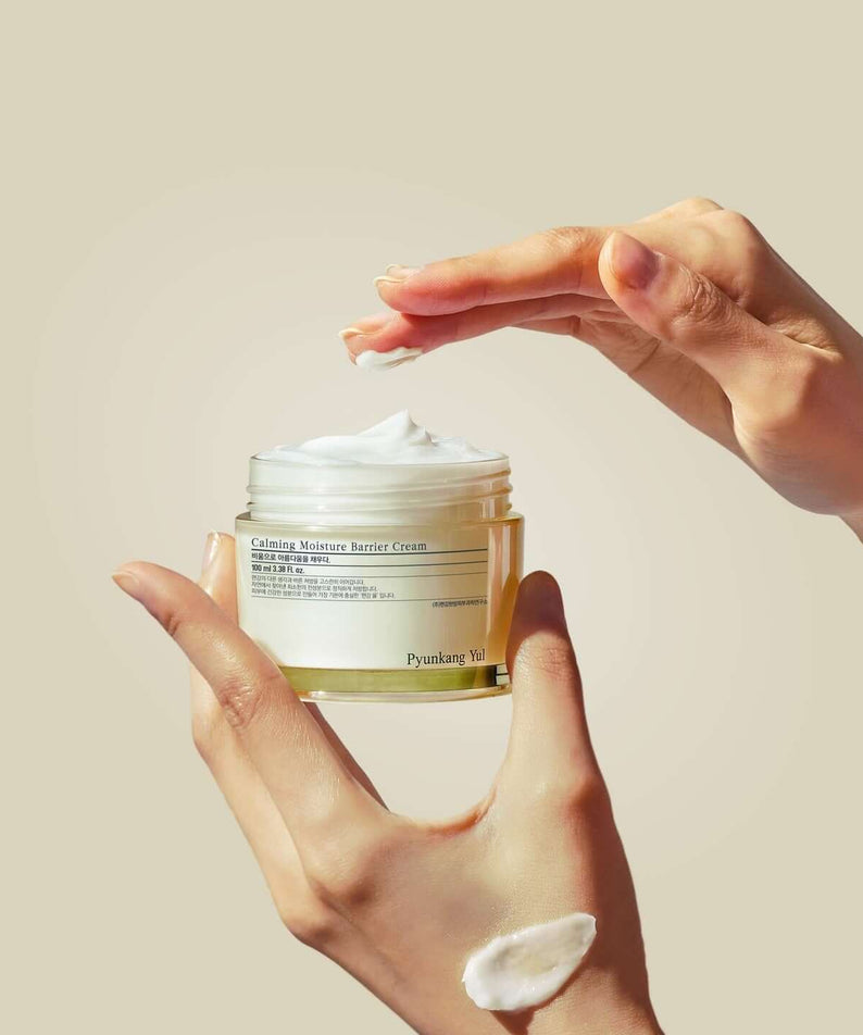Hands holding and applying PYUNKANG YUL Calming Moisture Barrier Cream 100ml from a jar.