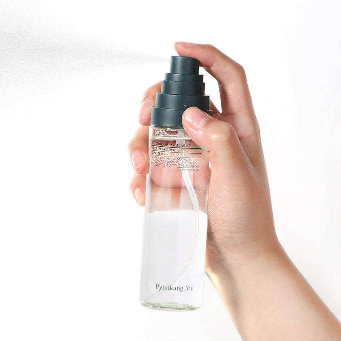 Hand holding PYUNKANG YUL Calming Moisture Mist 100ml spray bottle against white background, demonstrating product usage.