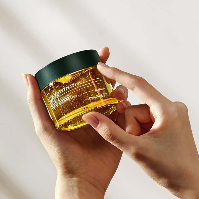 Hands holding PYUNKANG YUL Calming Relief Gel Wash-Off Pack 100g in a glass jar with green lid