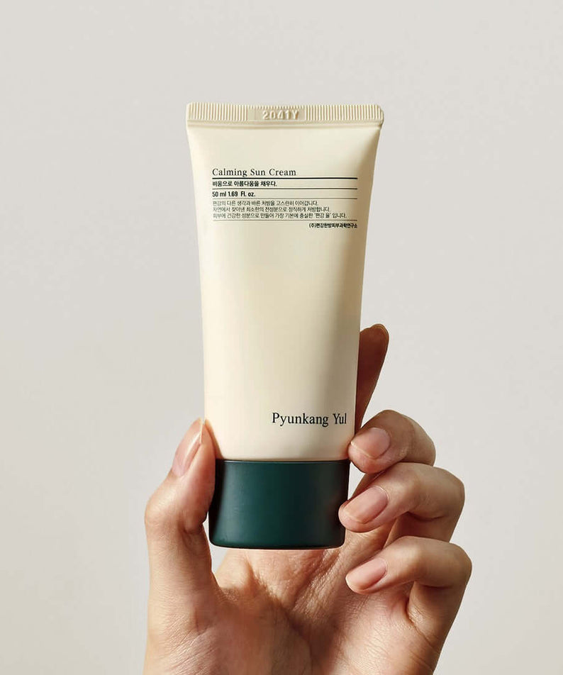 Person holding a tube of PYUNKANG YUL Calming Sun Cream SPF+PA++++ 50ml against a plain background.