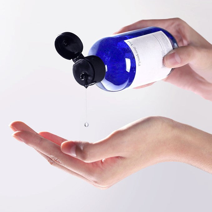 Hand applying PYUNKANG YUL Essence Toner from blue bottle, nourishing and hydrating skincare routine product.