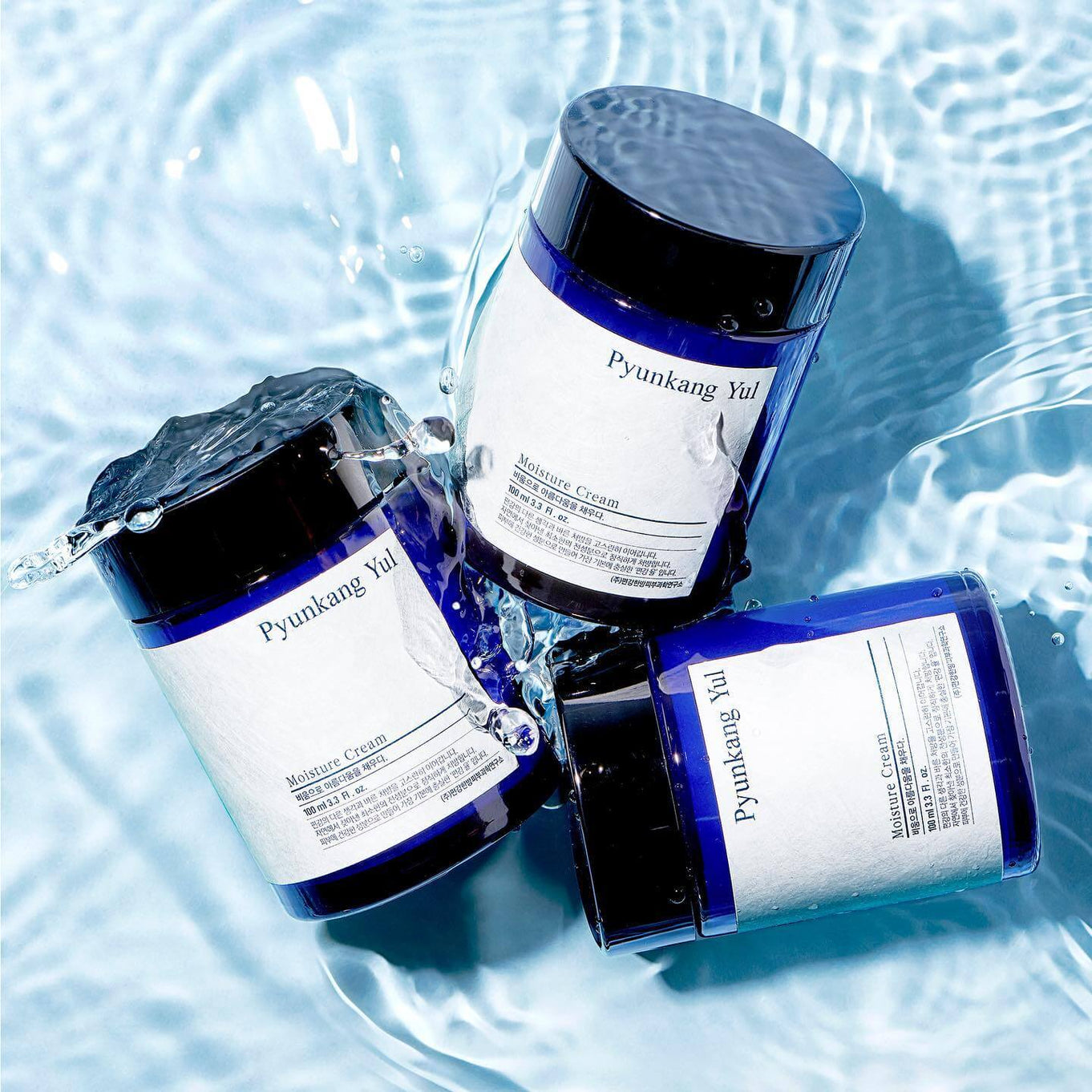 Three jars of PYUNKANG YUL Moisture Cream 100ml floating on water surface