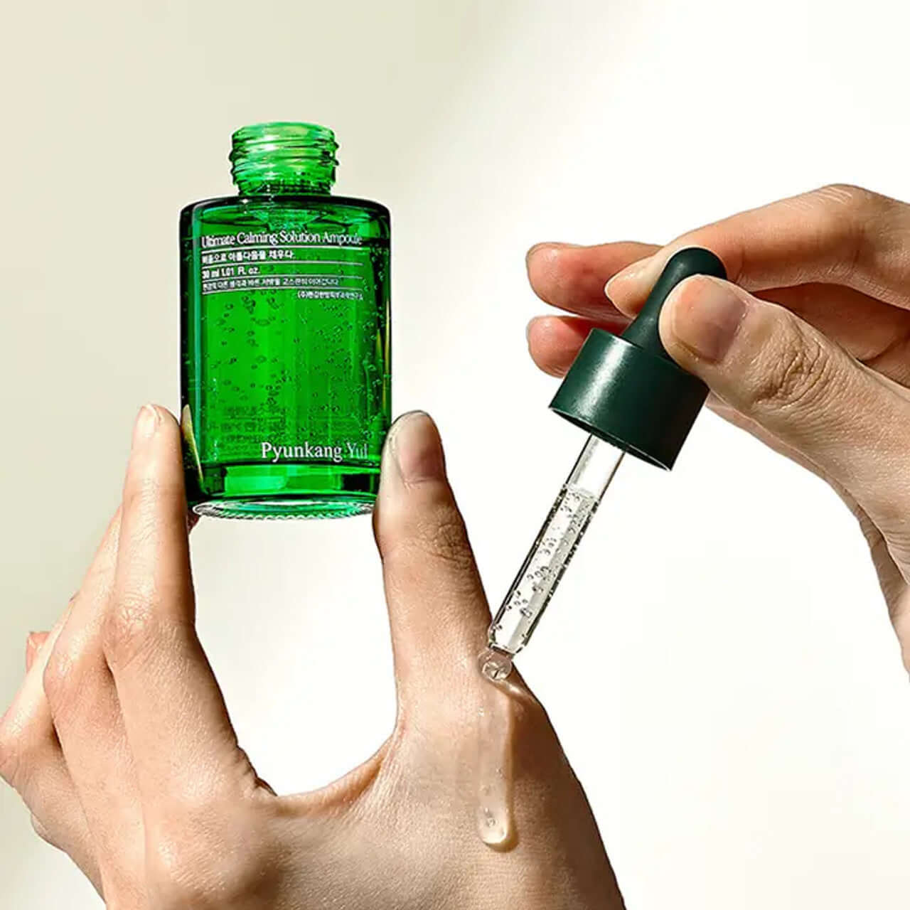 Hands pouring PYUNKANG YUL Ultimate Soothing Solution Ampoule 30ml from dropper bottle