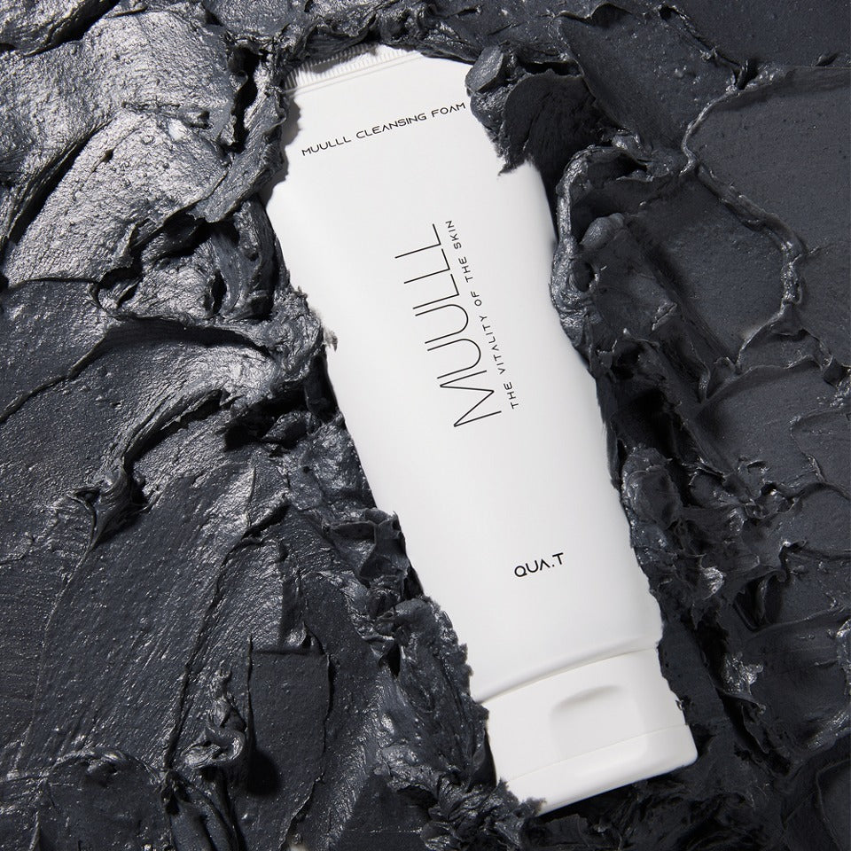QUA-T Cleansing foam 150g surrounded by gray clay-like texture, showcasing the cleansing power of the skincare product.