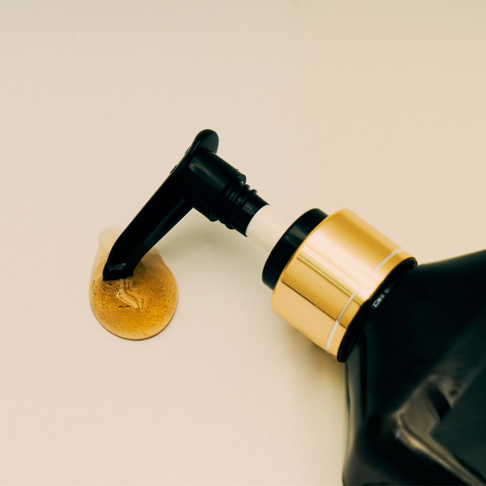 Close-up of QUA-T Samjin Out Oil 220ml bottle with pump dispenser and oil on a light surface.