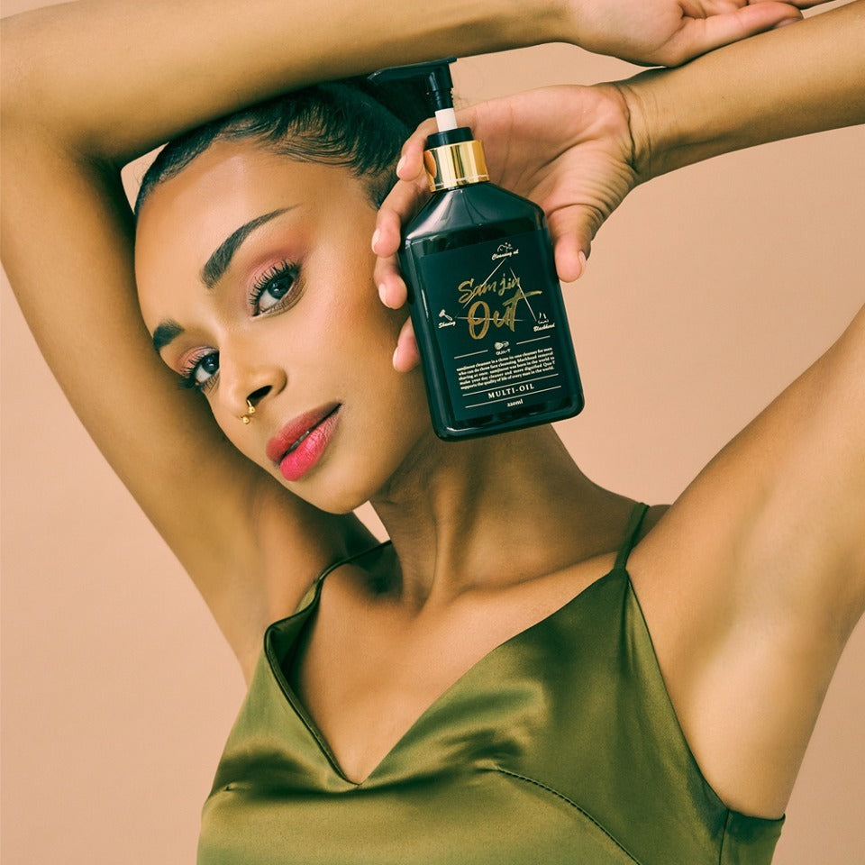 Woman holding QUA-T Samjin Out Oil 220ml against neutral background