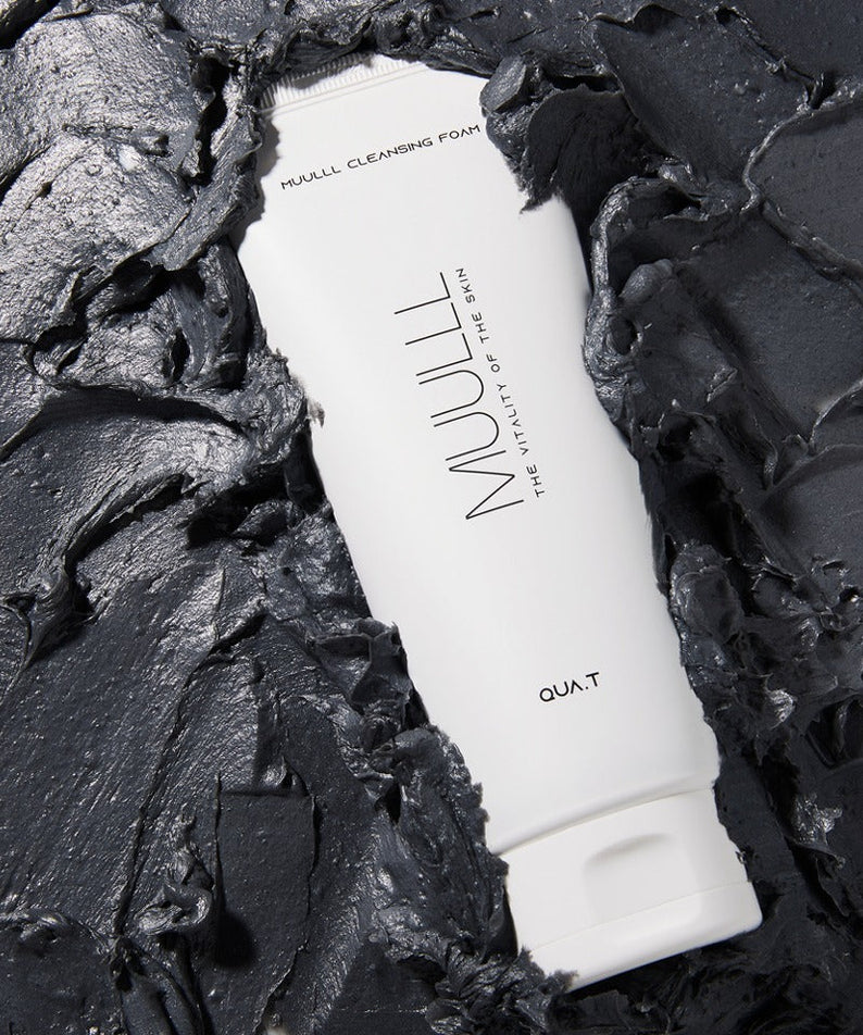 QUA-T Cleansing foam 150g surrounded by gray clay-like texture, showcasing the cleansing power of the skincare product.