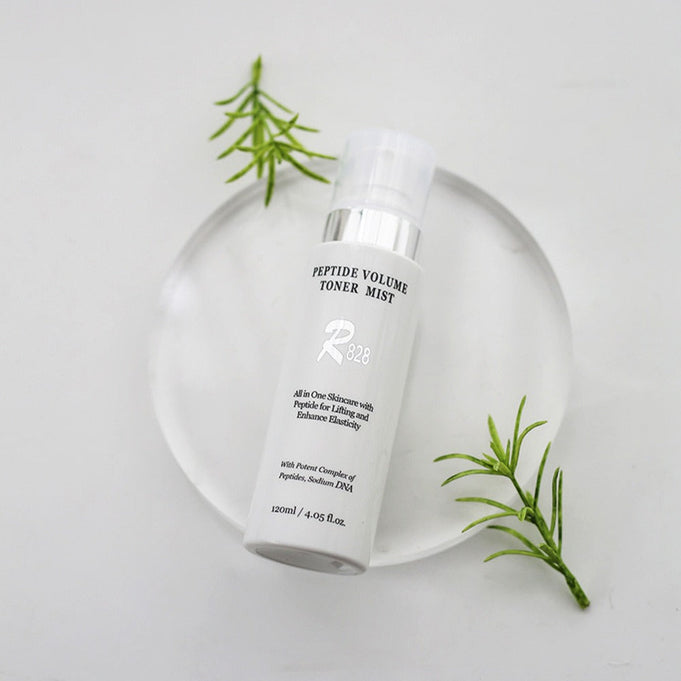 R828 Peptide Volume Toner Mist on a clear display with green leaves, 120ml bottle for skin care hydration and peptide infusion.