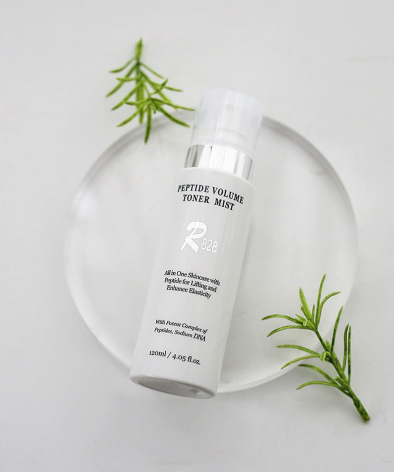 R828 Peptide Volume Toner Mist on a clear display with green leaves, 120ml bottle for skin care hydration and peptide infusion.