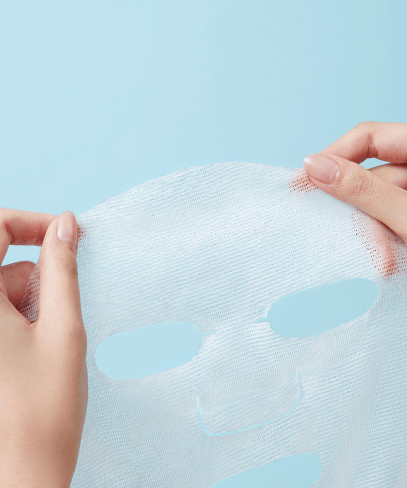 Person holding a REAL BARRIER Aqua Soothing Cream Mask sheet against a blue background.