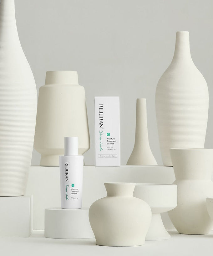 REJURAN Derma Healer Moisture Treatment Essence 70g bottle displayed among white ceramic vases.