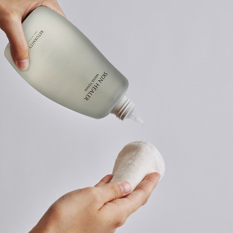 Person using RETURNITY Skin Healer Water Toner 300ml on a cotton pad for skincare routine.