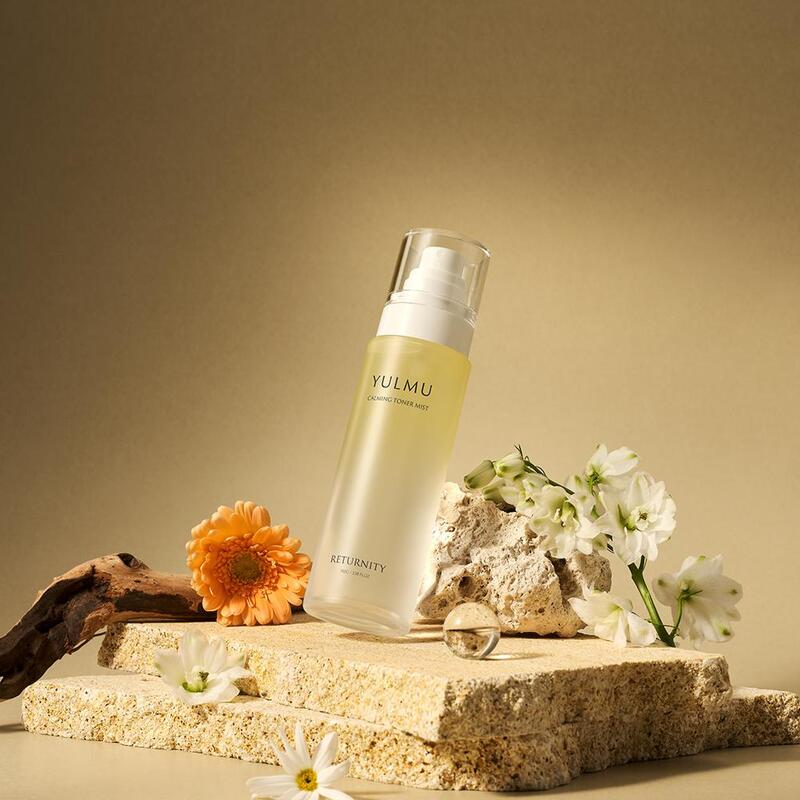 RETURNITY Yulmu Calming Toner Mist 100ml bottle surrounded by flowers on a textured stone surface.