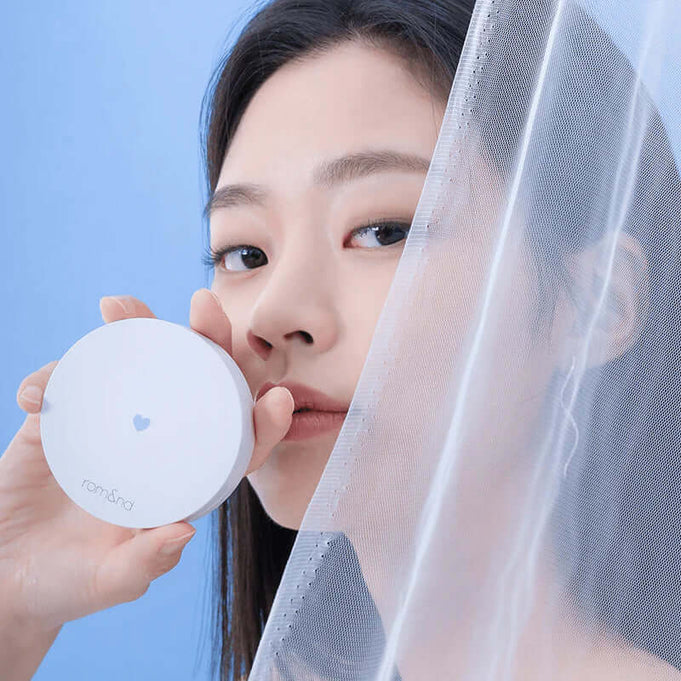 ROMAND Better Than Finish compact held by a person against sheer fabric backdrop