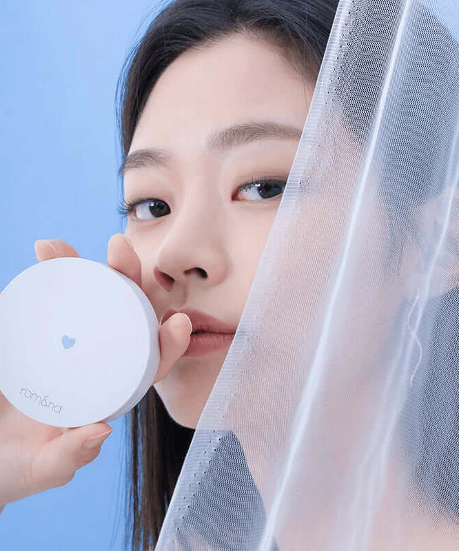 ROMAND Better Than Finish compact held by a person against sheer fabric backdrop