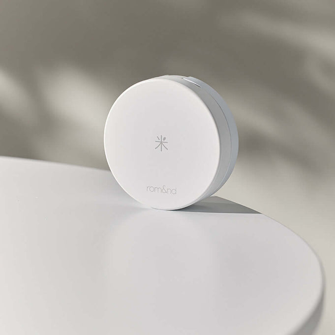 ROMAND white me tone up sun cushion on a white surface with soft shadow
