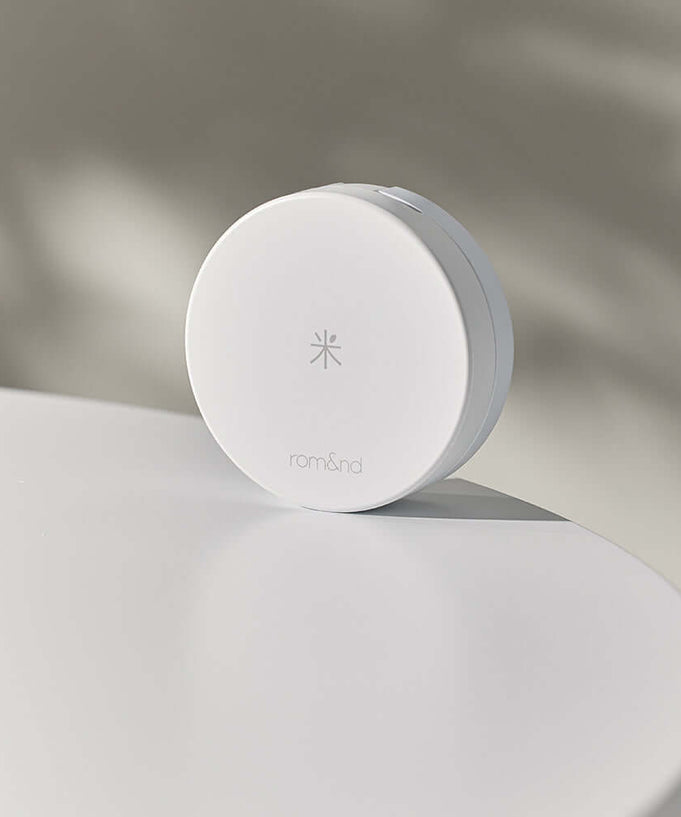 ROMAND white me tone up sun cushion on a white surface with soft shadow