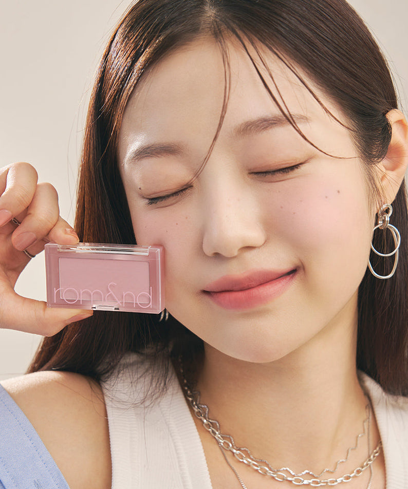 Smiling person holding ROMAND Better Than Cheek Blush next to their face