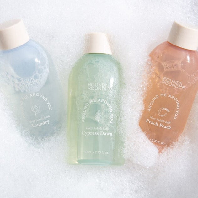 ROUND A'ROUND Hour Bubble Bath bottles surrounded by bubbles, showcasing scents like Cypress Dawn and Peach Peach.