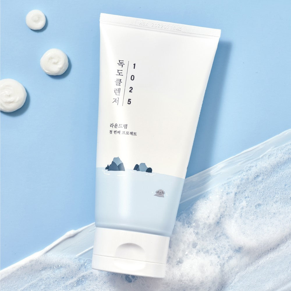 ROUND LAB 1025 Dokdo Cleanser 150ml tube on a textured background with foam spots.