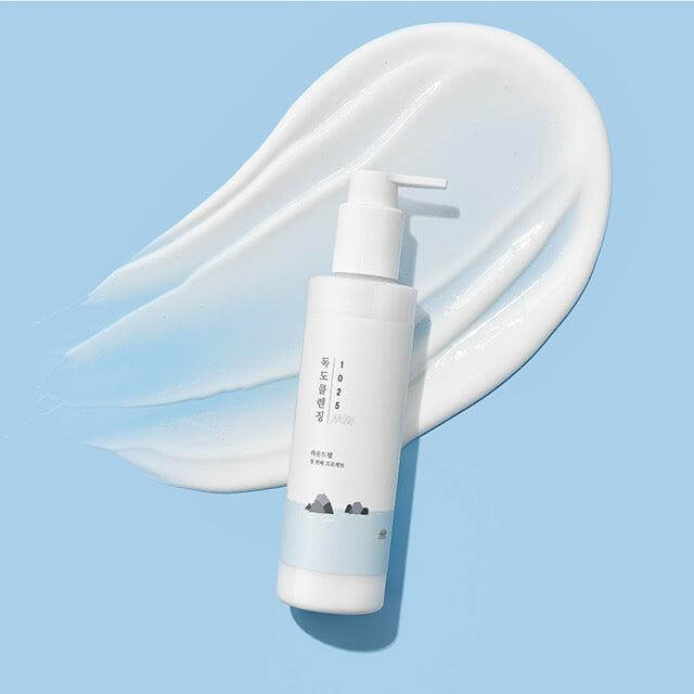Image of ROUND LAB 1025 Dokdo Cleansing Milk 200ml bottle on a blue background with product spread